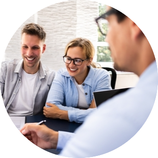 Beratung_rund Drei Personen sitzen an einem Tisch in einem modernen Büro und führen ein Beratungsgespräch. Auf dem Tisch liegen Unterlagen und ein Laptop, im Hintergrund sind helle Wände und ein Fenster zu sehen.