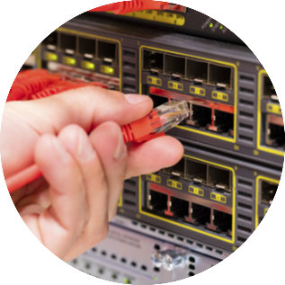 Netzwerktechnik_rund Hand steckt ein orangefarbenes Netzwerkkabel in einen Switch mit mehreren Ethernet-Ports. Die Geräte sind in einem Serverrack montiert, und die Ports sind mit gelben Markierungen versehen.